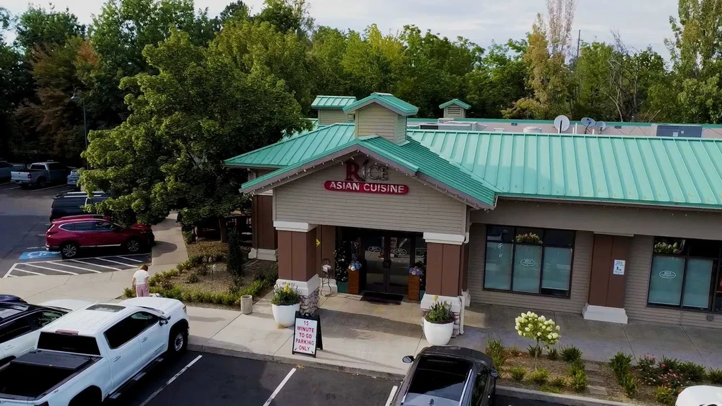 Daytime exterior of Rice Asian Cuisine with teal roof and parked cars.
