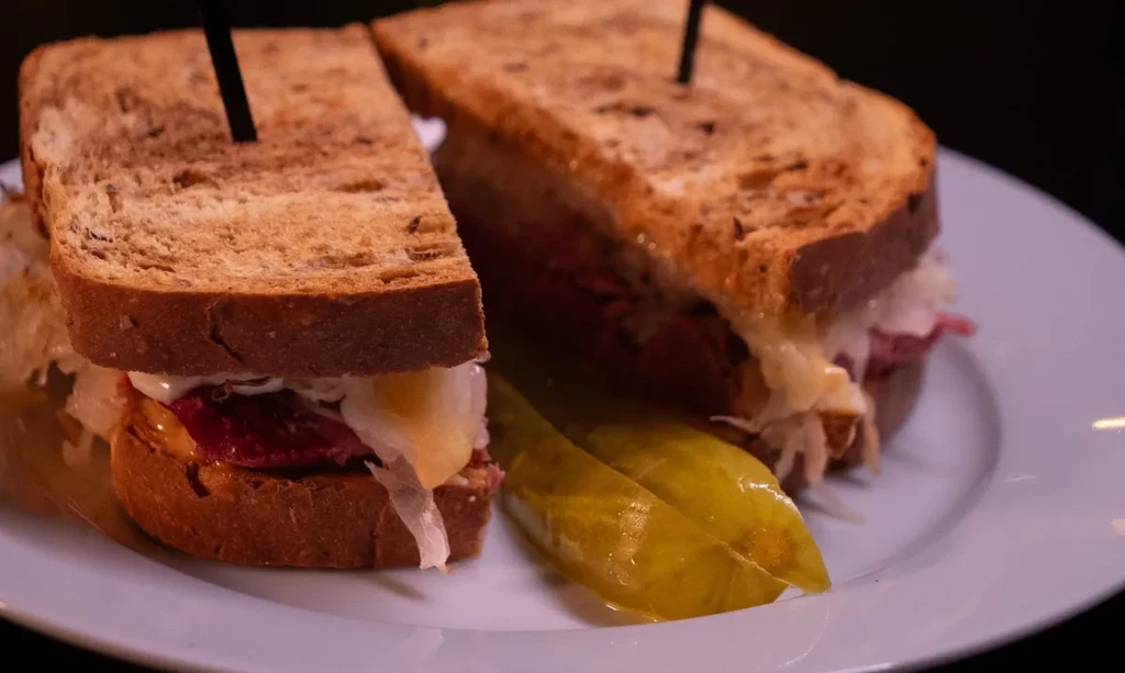 Reuben sandwich, cut in half, with a pickle spear on a plate.