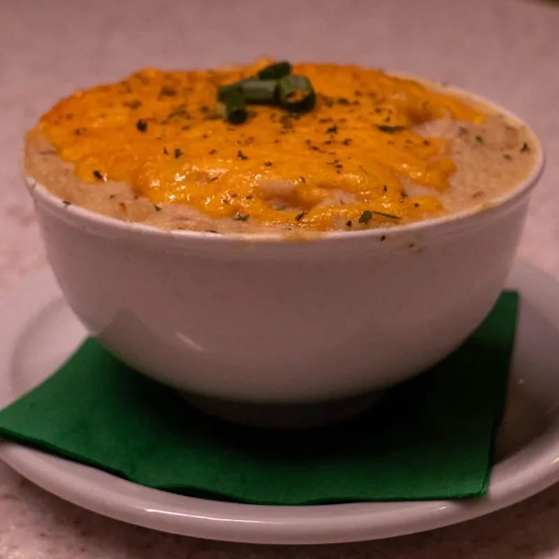 Close-up: Creamy dish topped with melted orange cheese and green herbs.