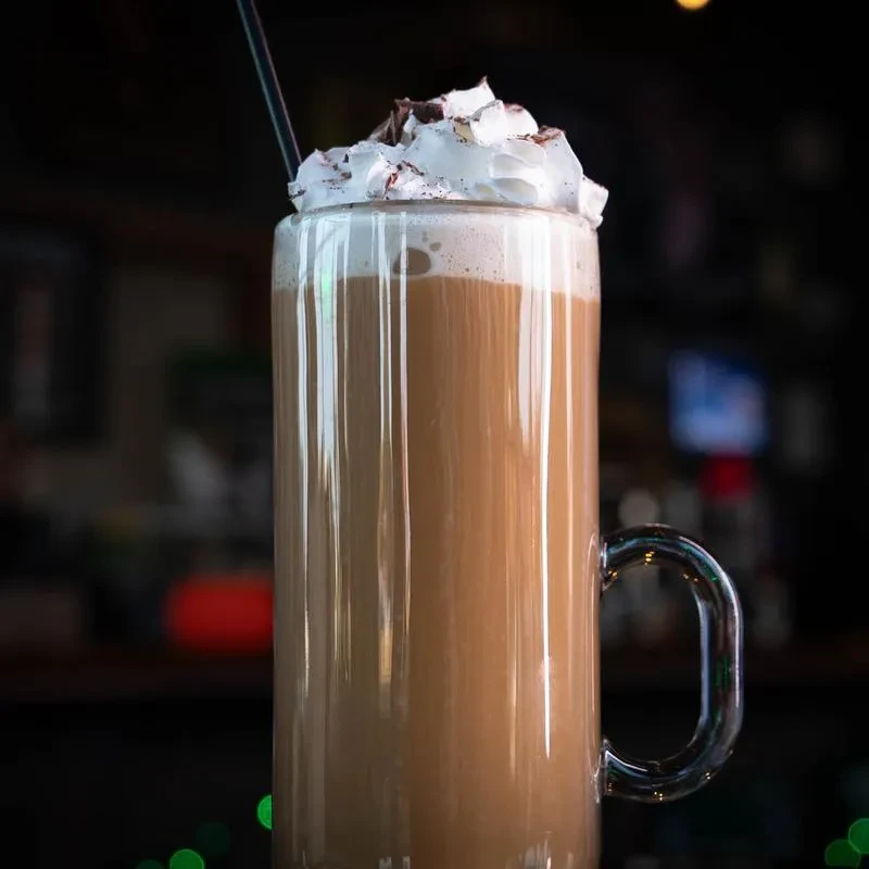 Glass mug of coffee/hot chocolate with whipped cream, chocolate shavings, straw.