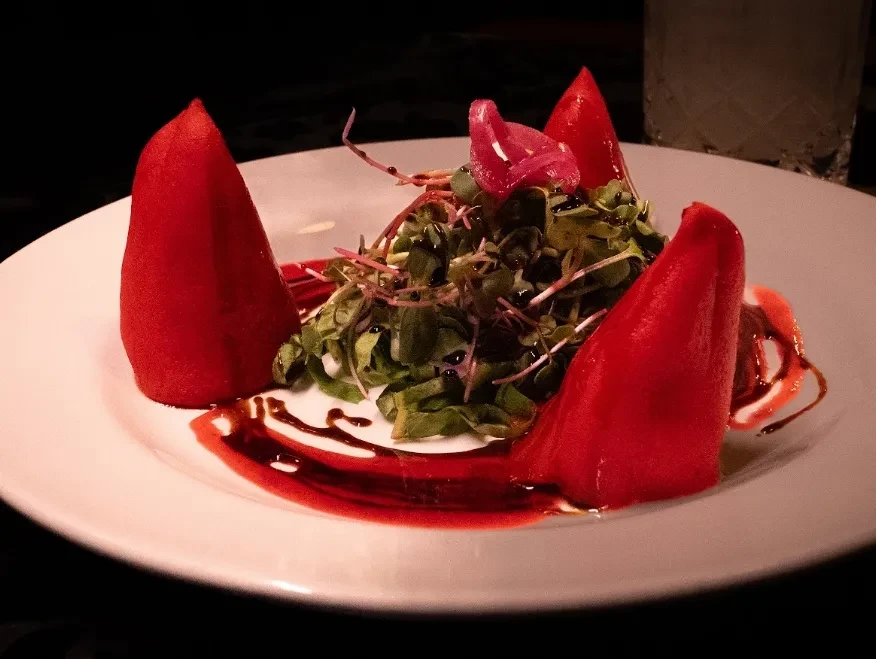 Gourmet dish: greens, red peppers, pickled onions, balsamic glaze on white plate.