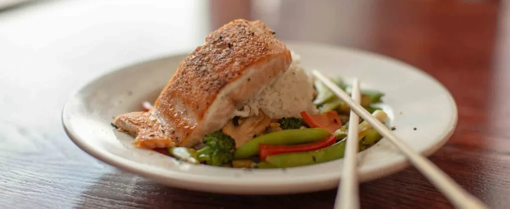 Plated salmon, white rice, colorful vegetables, and chopsticks.