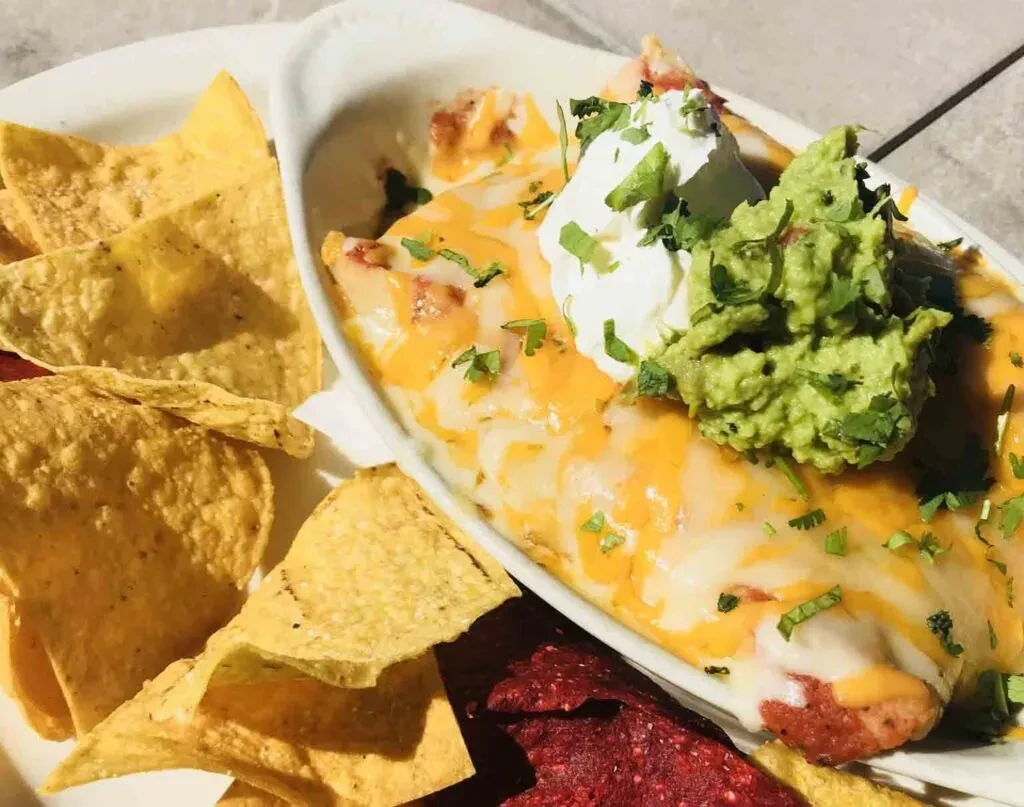 Cheesy baked casserole with guacamole, sour cream, cilantro, and chips.
