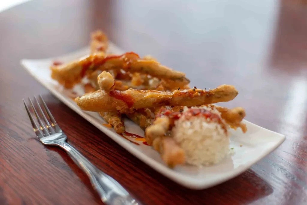 Fried vegetables, rice, and two sauces on a white plate with a fork.