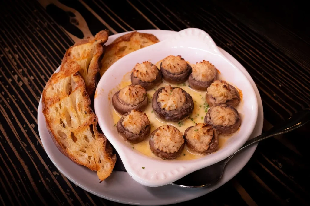 Plate of baked stuffed mushrooms with herbs and toasted baguette.