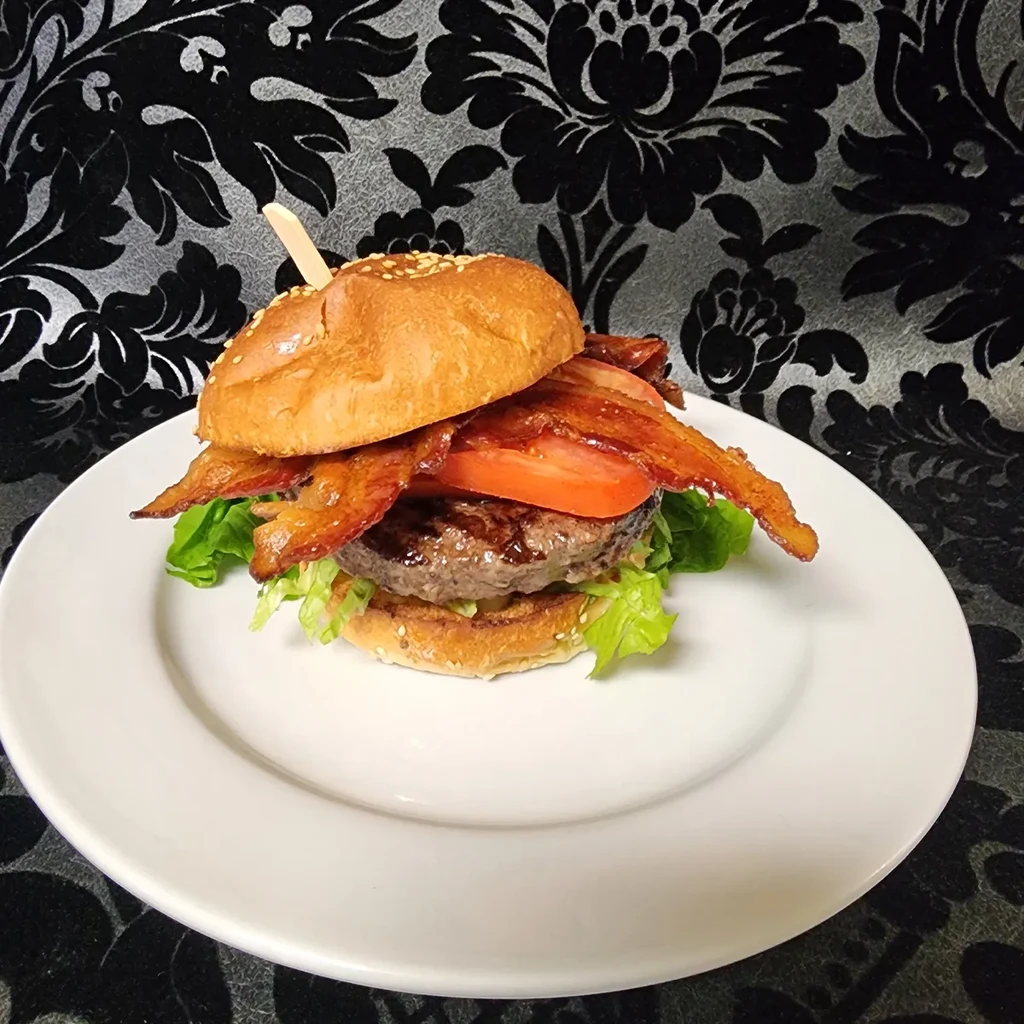 Skewered gourmet hamburger with bacon, lettuce, tomato on white plate.