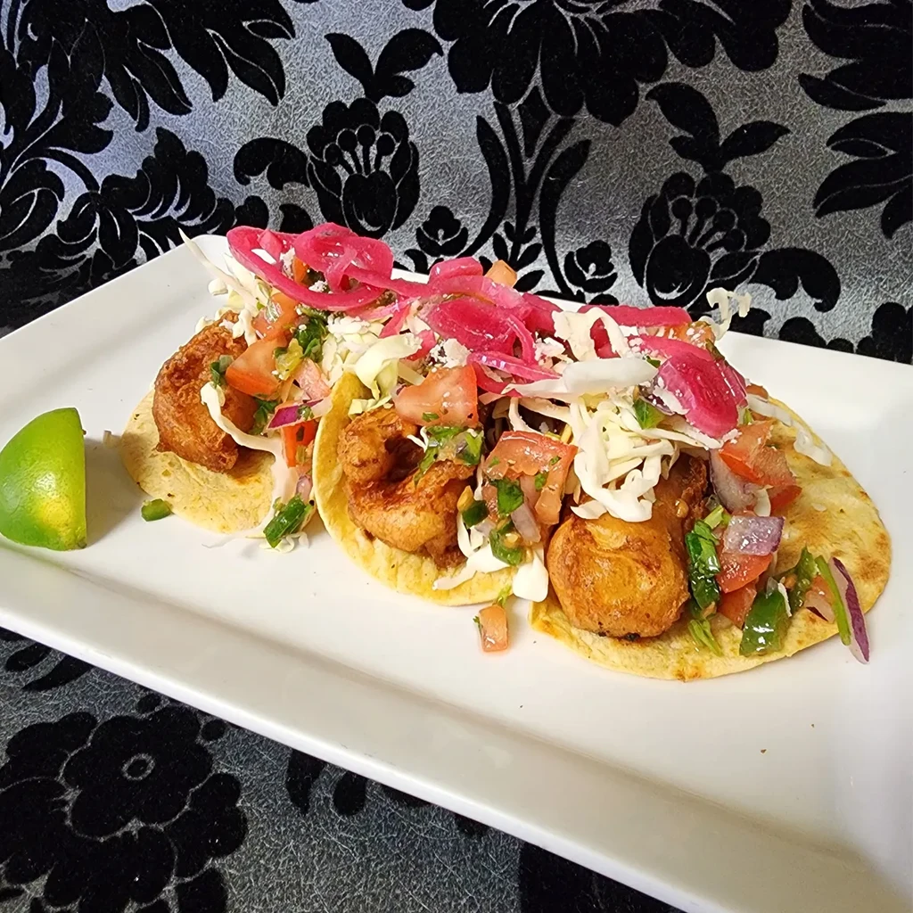 Three fried fish tacos with cabbage, tomatoes, cilantro, and pickled onions.