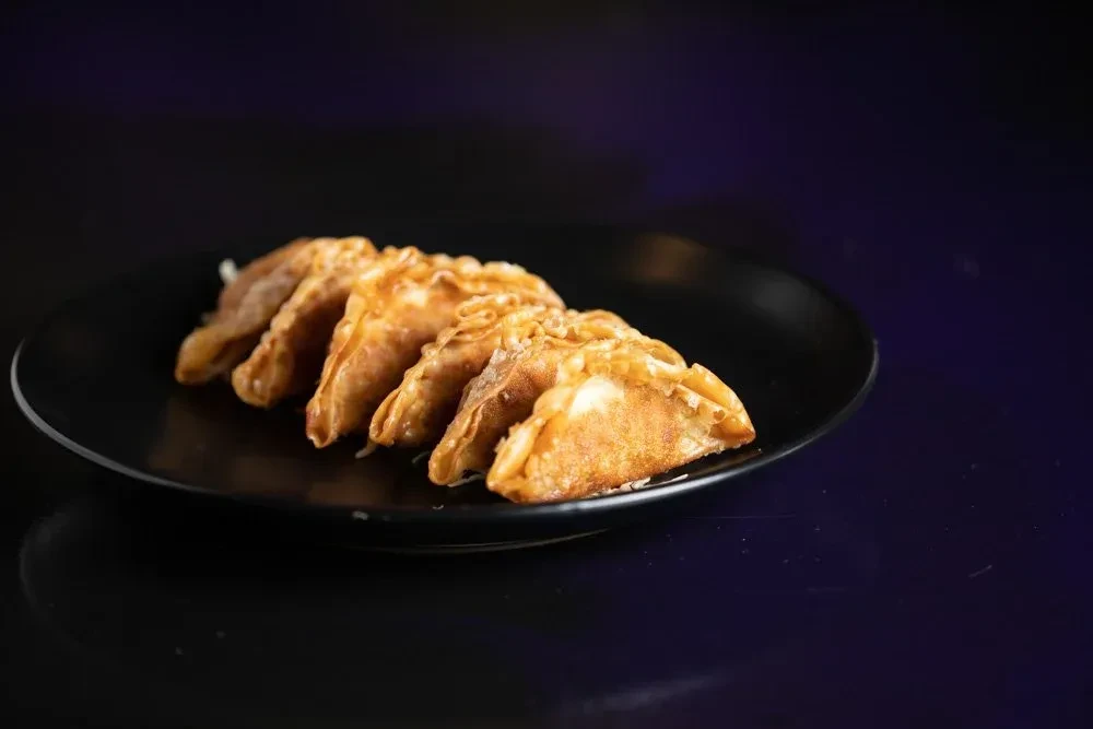 Five crispy golden-brown fried dumplings on a black plate with dark background.