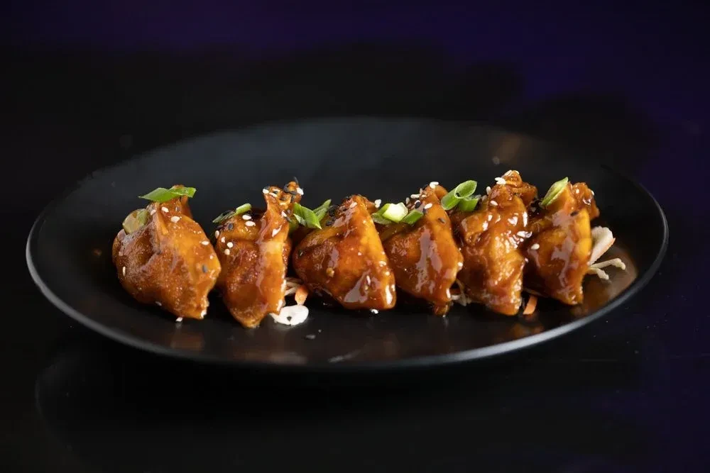 Six glazed chicken pieces with sesame, green onions, and shredded cabbage.