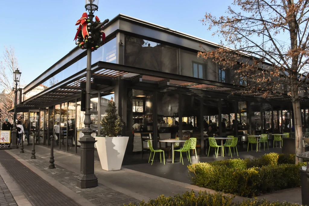 Modern glass-fronted restaurant with outdoor lime-green chairs and festive lamppost.