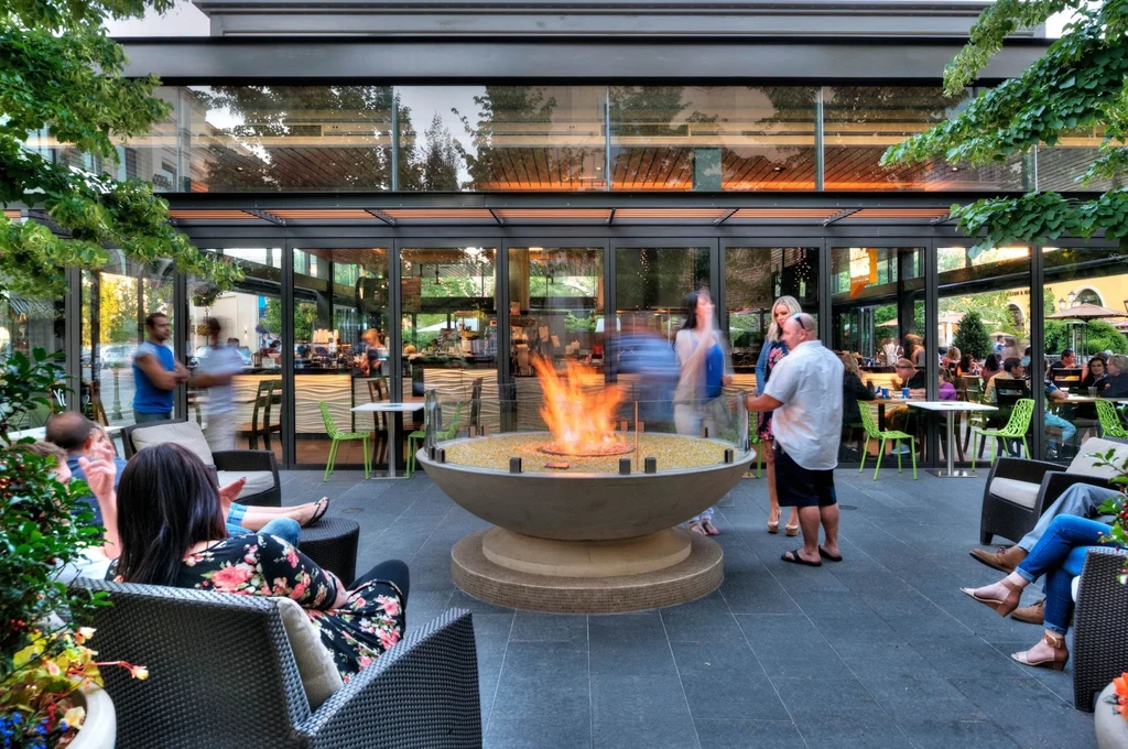 Modern restaurant patio with a glowing fire pit and socializing guests.