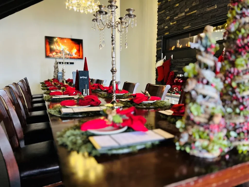 Long Christmas dining table with candelabras, garlands, and two fireplaces.