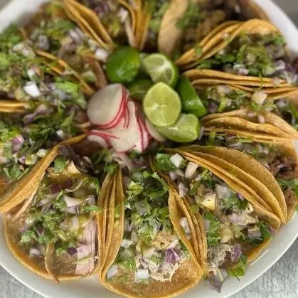 Tacos arranged circularly on a platter with lime and radishes.