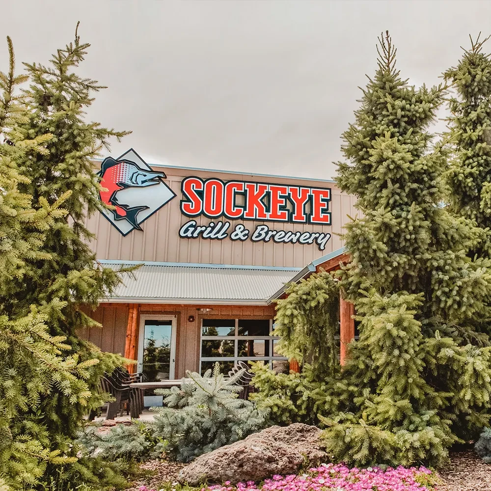 Exterior of Sockeye Grill & Brewery with salmon logo and lush trees.