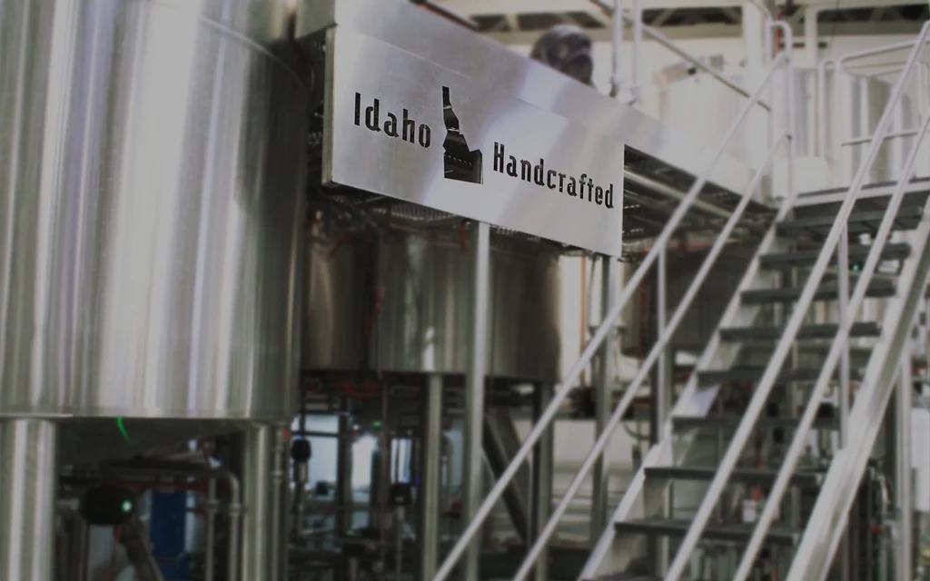Industrial brewery with stainless steel tanks and "Idaho Handcrafted" sign.