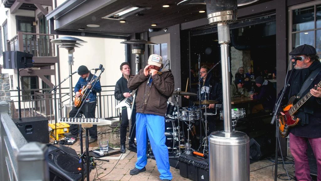 A five-person band performs outdoors on a snowy patio at a restaurant.
