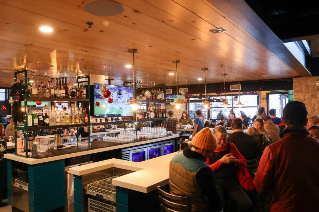 Lively, well-stocked bar interior with people, sports on TV, and holiday decor.