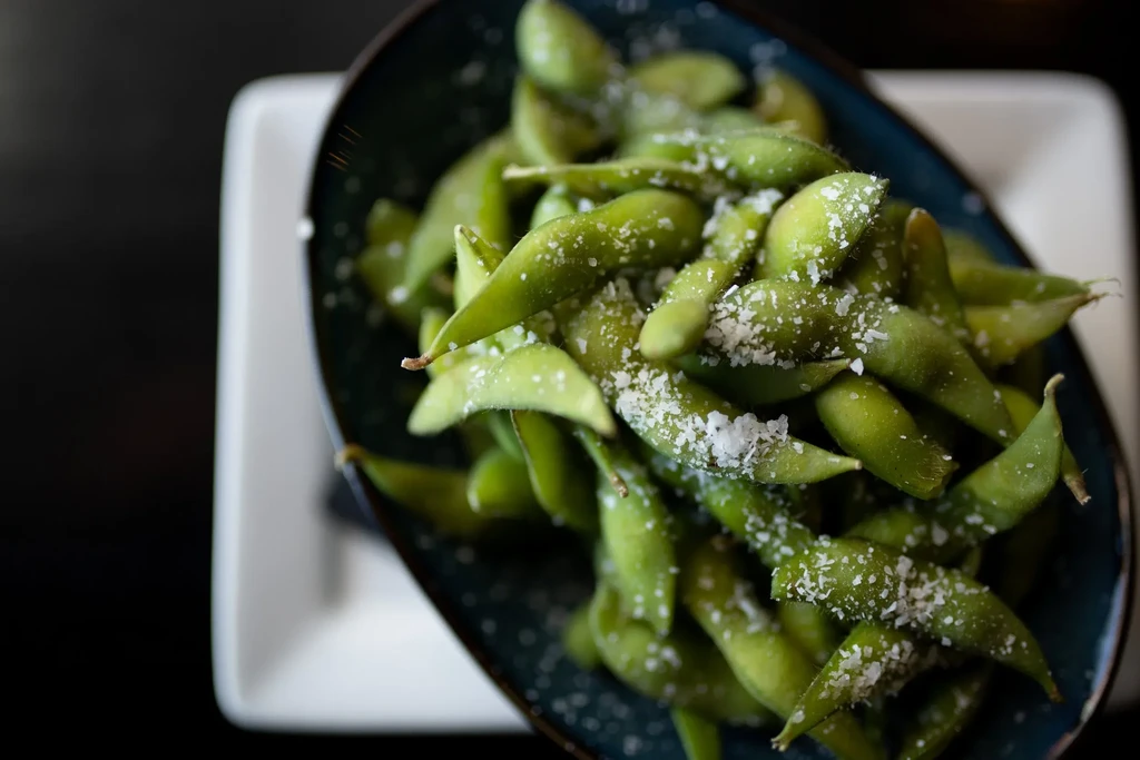 Green edamame pods sprinkled with coarse sea salt in a dark bowl.