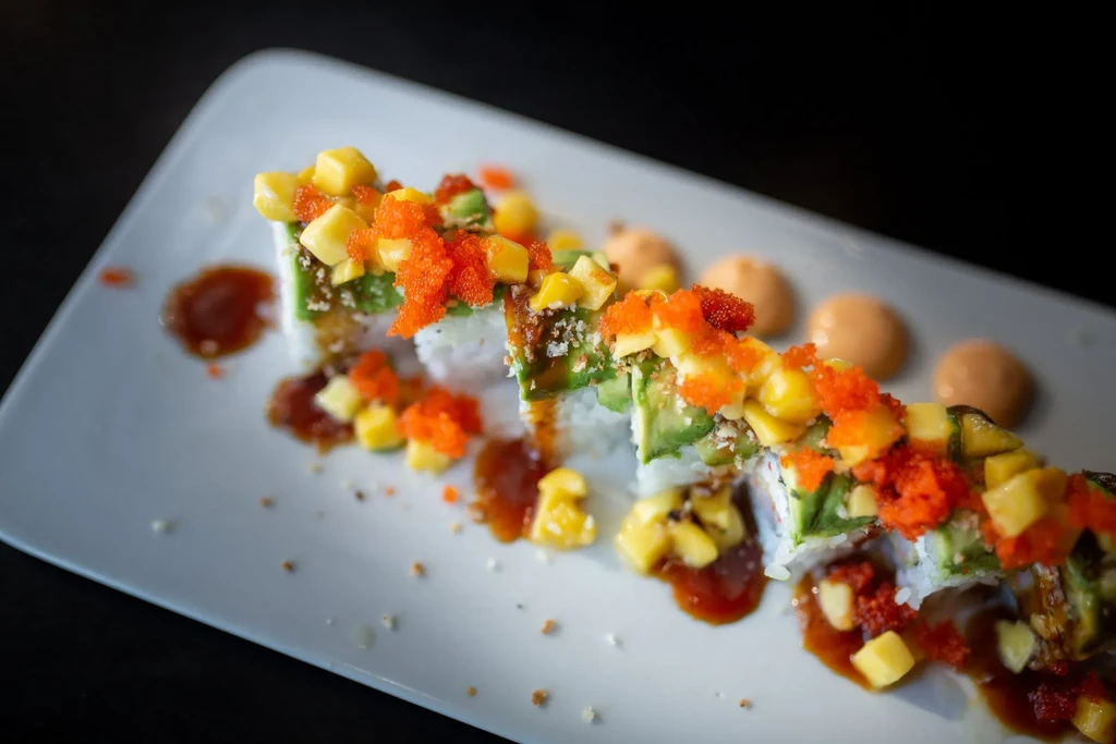 Plate of sushi rolls with mango, avocado, roe, and dark sauce.