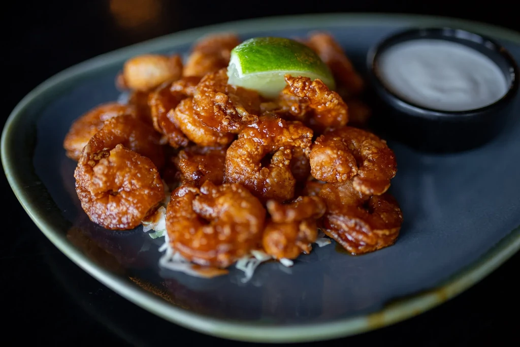 Fried shrimp in reddish sauce on garnish, with lime and dipping sauce.