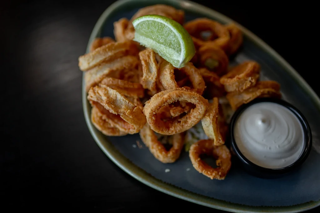 Deep-fried golden rings with lime wedge and dipping sauce on a plate.
