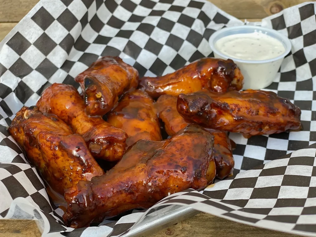 Heavily sauced chicken wings with creamy dip in a metal tray.
