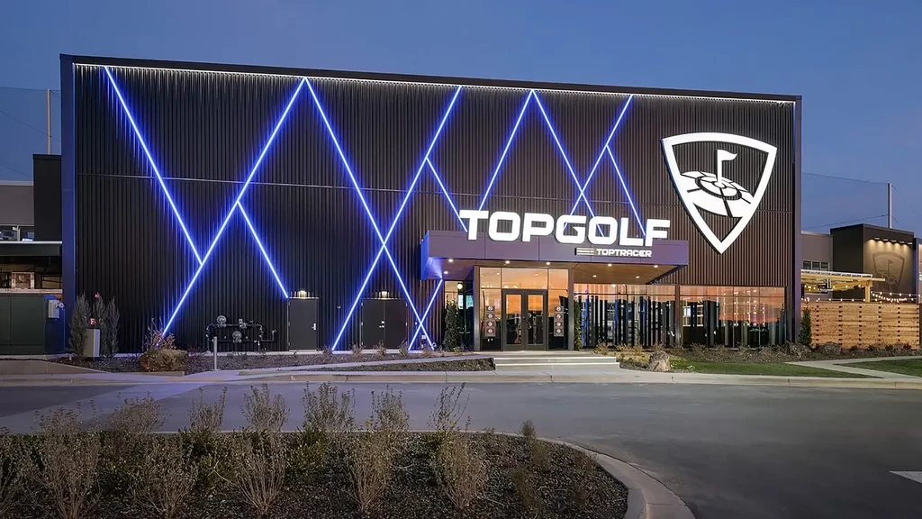 Exterior of Topgolf building with blue crisscross lights at dusk.