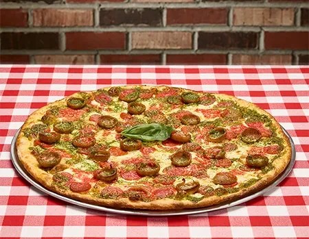 Pepperoni, mushroom, pesto, and basil pizza on checkered cloth.