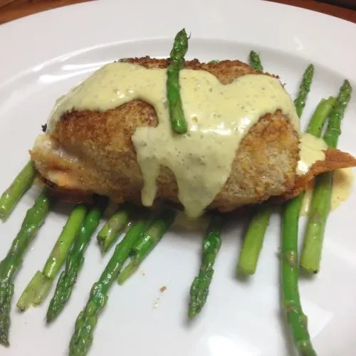 Breaded entree with cream sauce and green asparagus on a white plate.