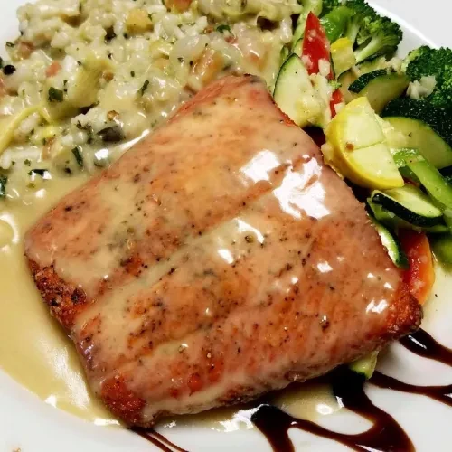 Plated pan-seared fish with creamy sauce, risotto, and vibrant vegetables.
