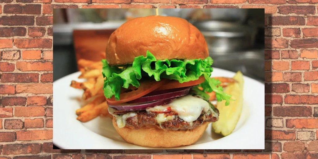 Well-stacked cheeseburger, fries, and pickle spear on a white plate.
