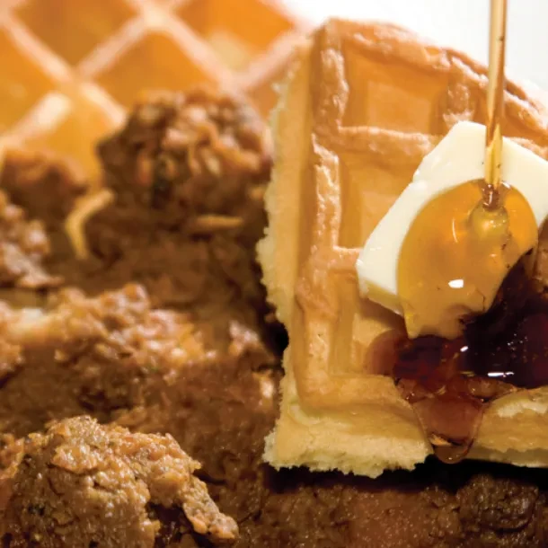 Close-up of golden waffle with melting butter, syrup, and fried chicken.