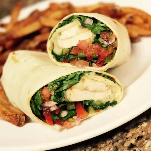 Halved chicken and vegetable wrap on a plate with fries.