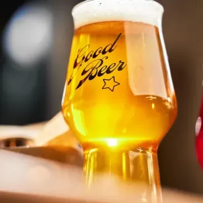 Amber beer in a "Good Beer" glass with white foam and mist.
