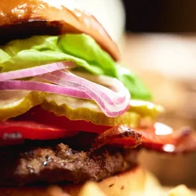 Close-up of a gourmet layered burger with beef, bacon, and vegetables.