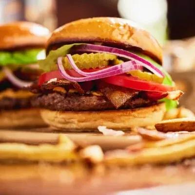 Gourmet hamburger with bacon, vegetables, and fries on a wooden board.