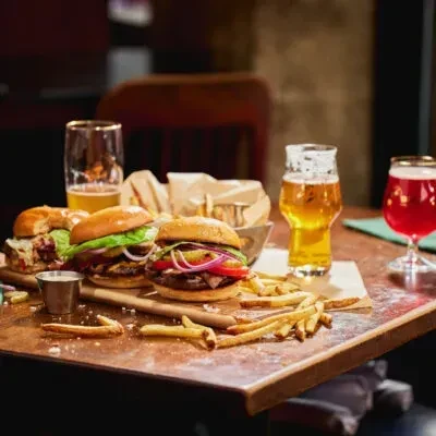 Three gourmet burgers, fries, two beers, and a red drink.