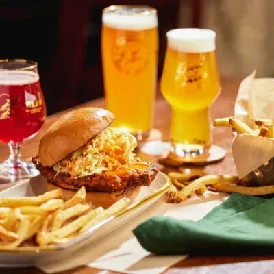 Fried chicken sandwich, coleslaw, fries, and three drinks on a table.