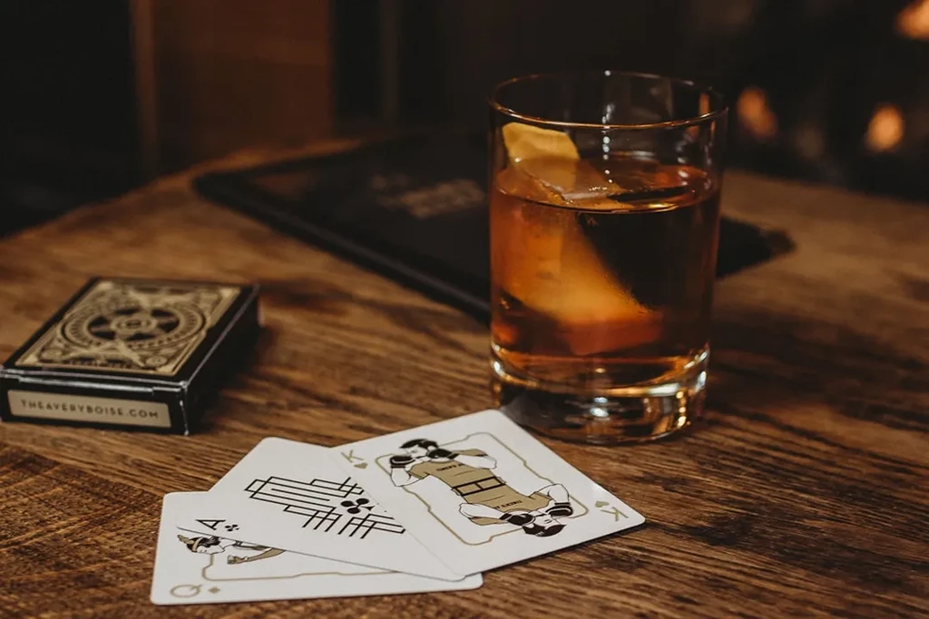 Cocktail, unique boxer playing cards, and card box on wood.