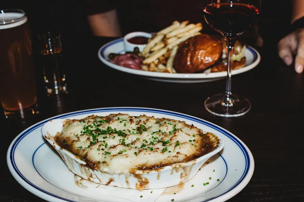 Baked savory pie, burger, fries, beer, and red wine on dark table.