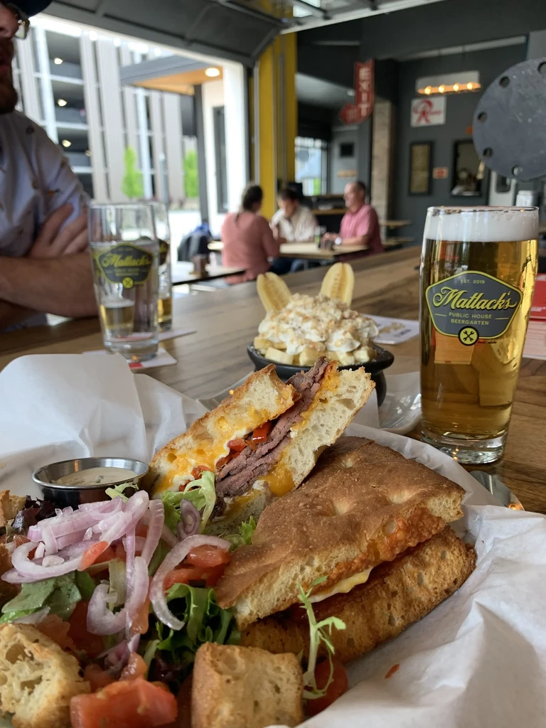 Matlack's focaccia sandwich, salad, beer, and banana pudding on a table.