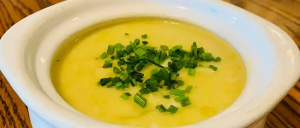 Creamy light yellow soup with green chives in a white bowl.