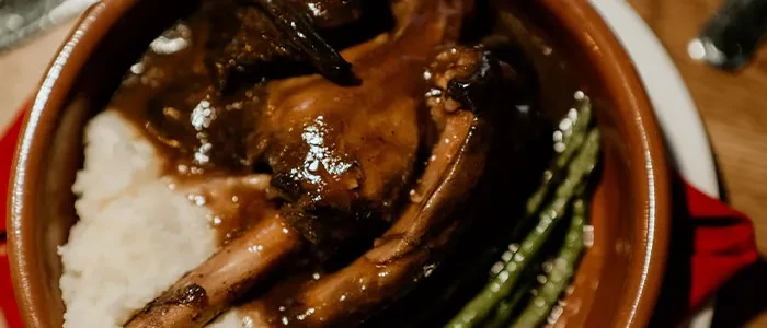 Rustic bowl of braised meat, mashed potatoes, and green vegetables.