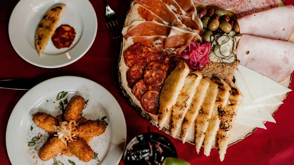 Top-down view of a lavish charcuterie board, croquettes, and drink.