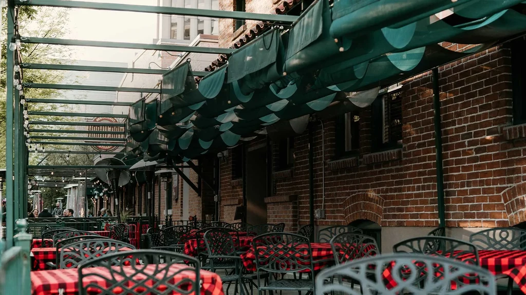 Restaurant patio with red and black checkered tables and green pergola.