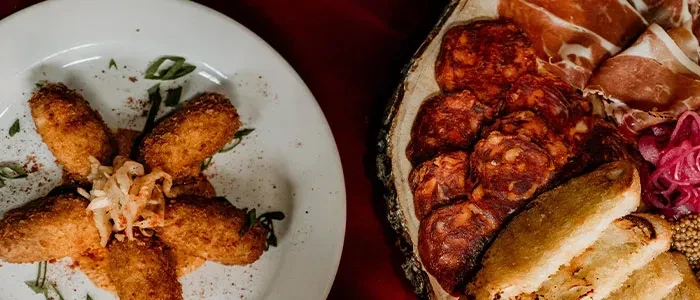 Close-up overhead: golden breaded items and a wooden platter of cured meats.