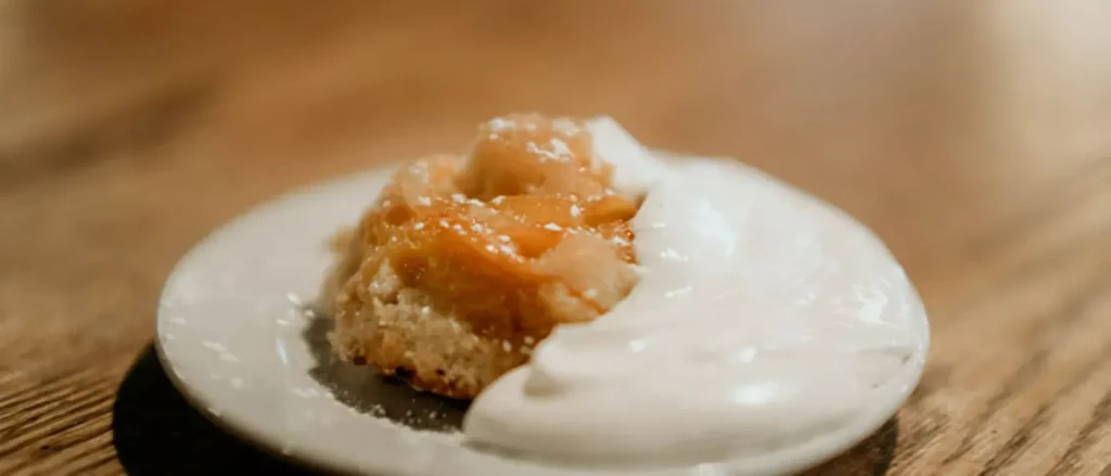 Golden-brown baked dessert with caramelized fruit, powdered sugar, whipped cream.