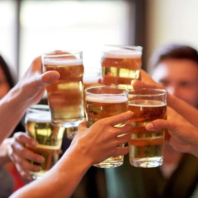 Five hands toasting with frothy beer in clear glasses.