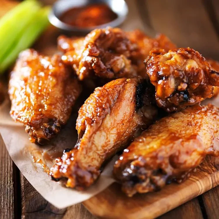 Piled chicken wings with dark, glossy sauce on parchment and wood.