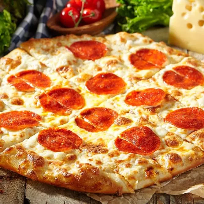 Freshly baked pepperoni pizza, sliced, on a wooden surface with ingredients.